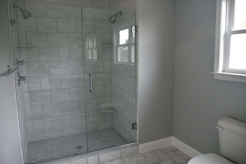 Shower with two shower heads and glass doors, gray tiles for sleek modern look.